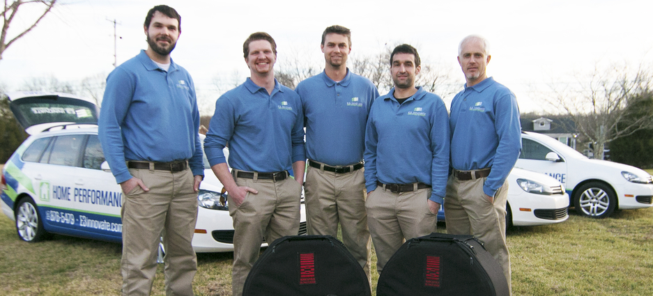 Five E3 INNOVATE team members standing in a field in front of company vehicles.